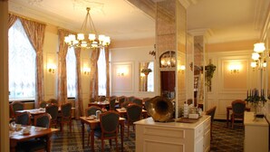 A hotel dining area with multiple tables and chairs, a central bar area, and decorative wall sconces. - Milbor Hotel (Bad Soden am Taunus)