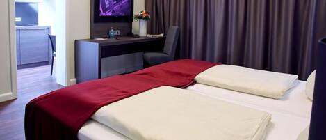 A hotel room with two beds, a desk with a TV, and a view of the hallway.