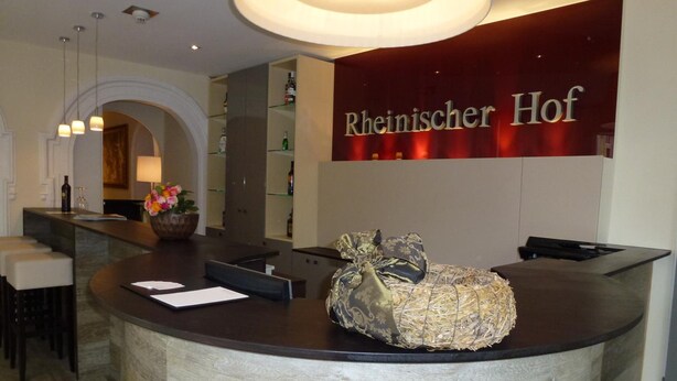 A reception area with a curved counter, a flower vase, and a sign reading "Rheinischer Hof". - Milbor Hotel (Bad Soden am Taunus)