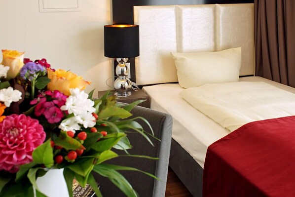 A hotel room with a bed, a nightstand with a lamp, and a floral arrangement. - Milbor Hotel (Bad Soden am Taunus)