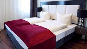 A neatly made bed with a red blanket, a white duvet, and two pillows. There are two bedside lamps on either side of the bed. - Milbor Hotel (Bad Soden am Taunus)