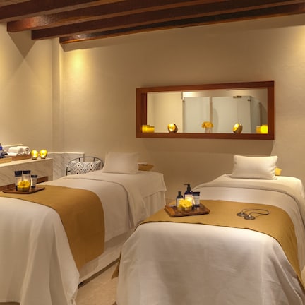 A hotel room with two beds, a large mirror, and a vanity with toiletries.