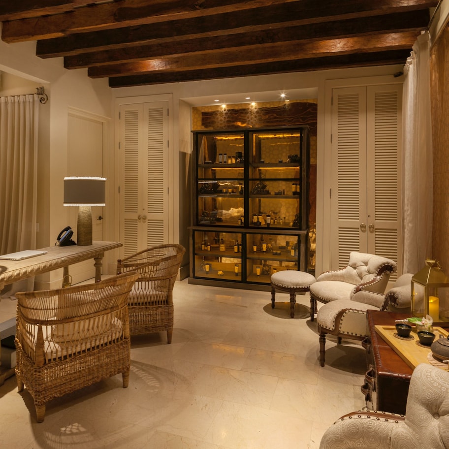 A spacious living room with a high ceiling, wooden beams, wicker furniture, and a glass display cabinet.