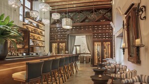 Un área de bar con sillas de madera, una barra con botellas y candelabros de cristal colgantes.