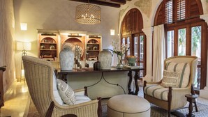 A room with wicker furniture, a chandelier, and a view of palm trees through large windows.