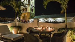 A rooftop terrace with wicker furniture, a table set for dining, and a bell tower in the background.