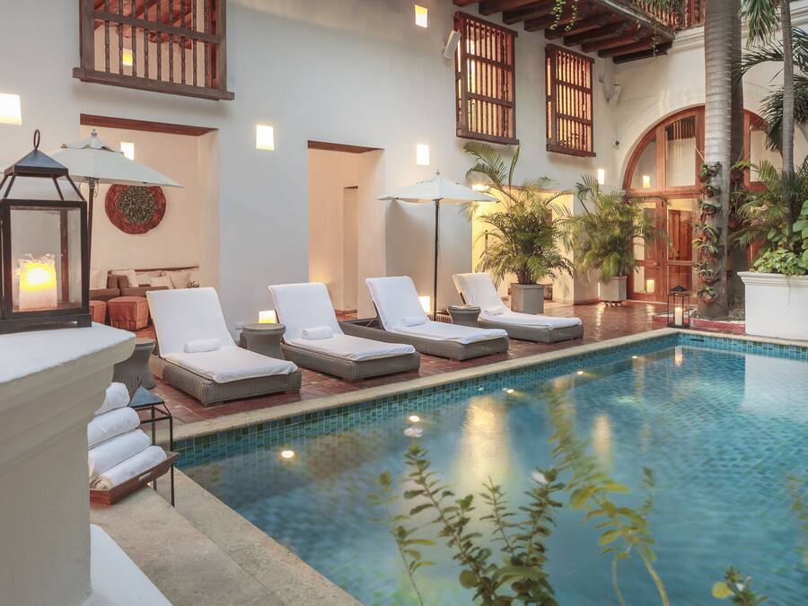 Uma área de piscina com espreguiçadeiras, um candeeiro e plantas em vasos.