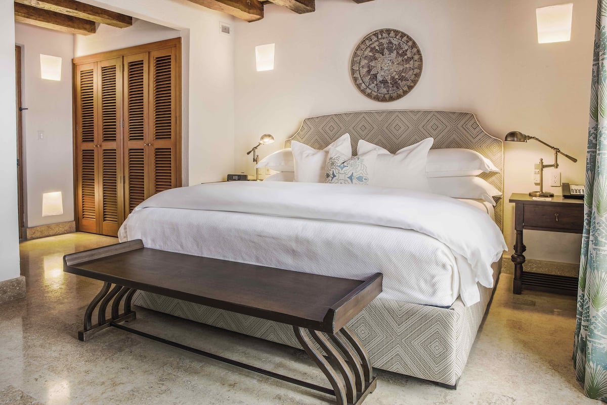 Camera da letto con un letto grande, comodini, una panca, armadio in legno e un elemento decorativo a parete.