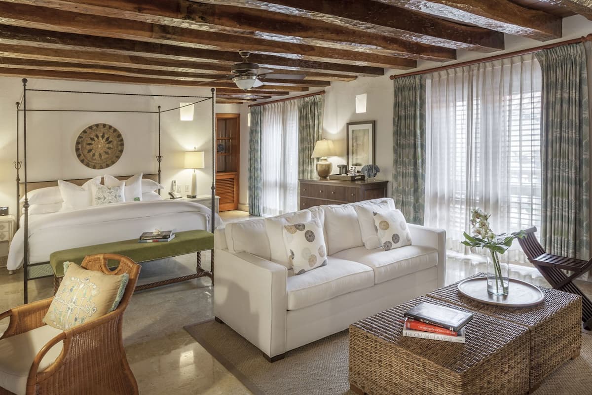 Una camera d'albergo con un letto, un divano, un tavolino in vimini e una sedia.