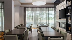 Un salón de conferencias con una larga mesa y sillas, chimenea, televisor montado en una pared de piedra y ventanas amplias con cortinas translúcidas.