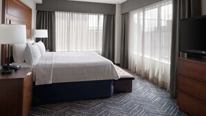 Habitación de hotel con una cama grande, un televisor de pantalla plana, un escritorio con lámpara y un ventilador de techo.