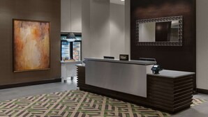 Una zona de recepción moderna de hotel con un gran cuadro abstracto, un mostrador de recepción, un minibar y un espejo grande en la pared.