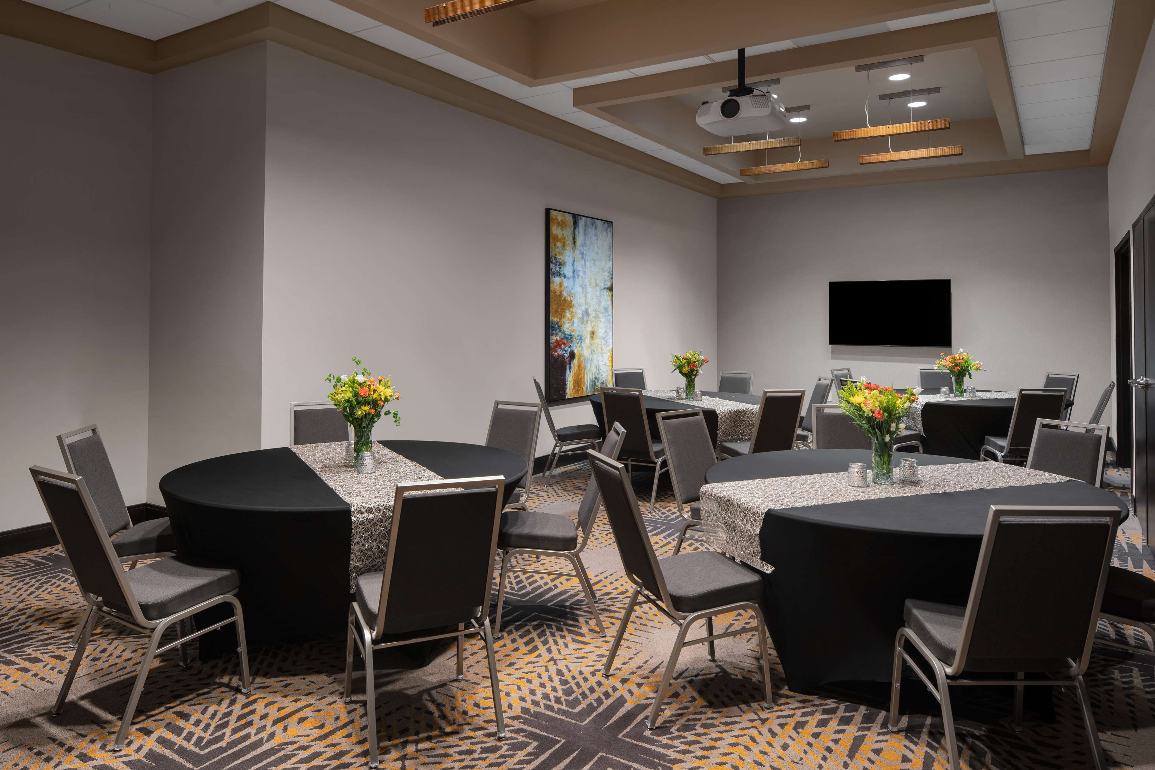 A conference room with round tables, chairs, a projector, and a large screen.