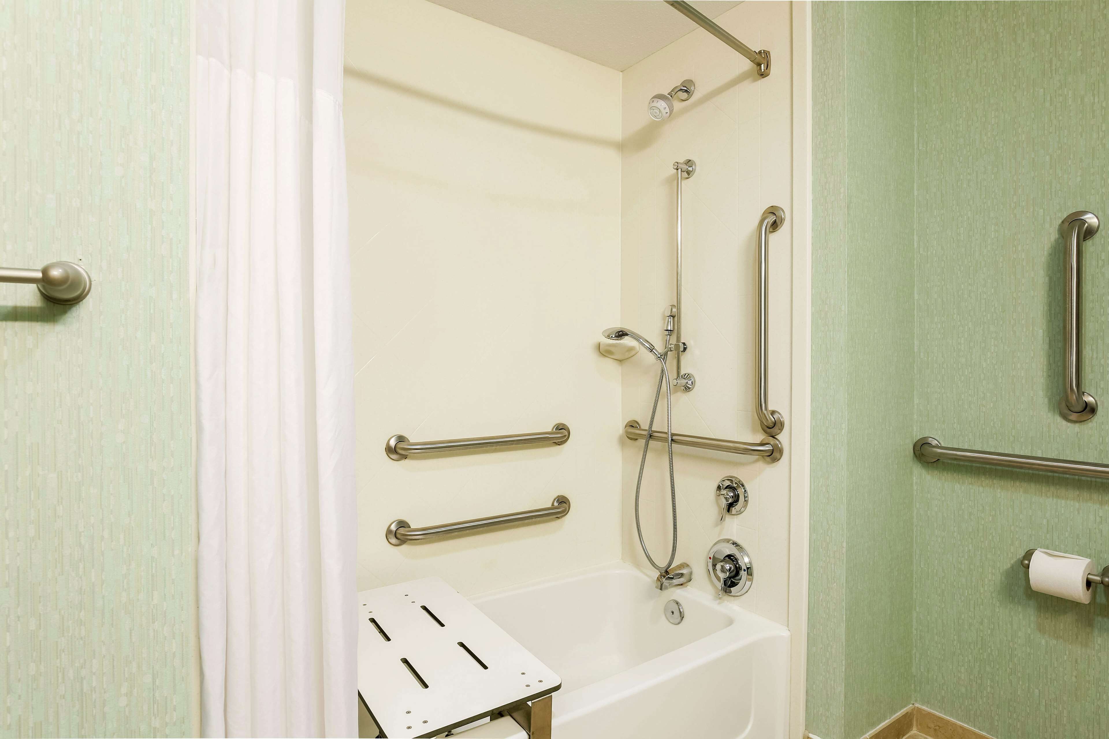 A bathroom with a shower, grab bars, a toilet, and a bathtub.