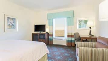 A hotel room with a bed, a desk with a television, a chair, and a window with curtains.