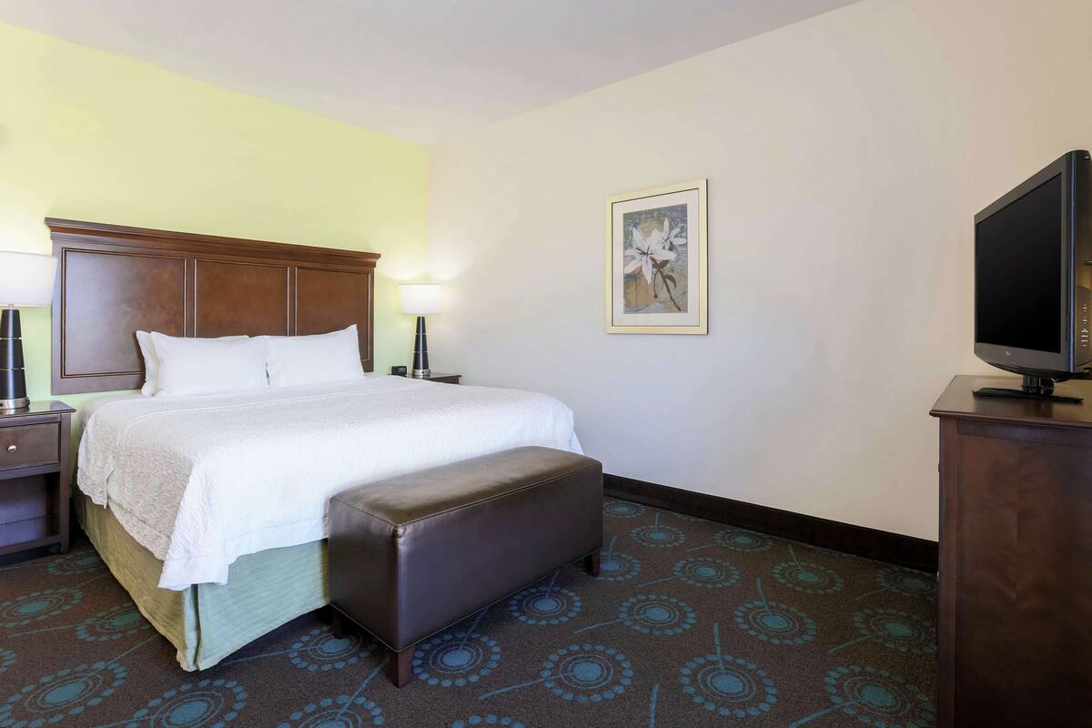 A hotel room with a bed, a nightstand, a lamp, a television, and a wall-mounted artwork.