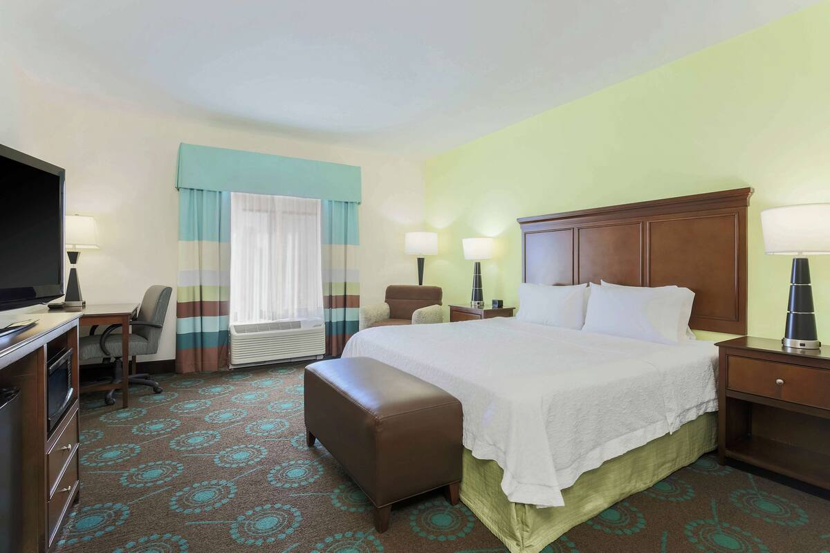 A hotel room with a bed, a desk, a chair, a TV, and a window with curtains.