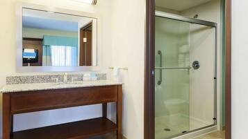 A bathroom with a granite countertop sink, a wooden vanity, a mirror, and a glass-enclosed shower.