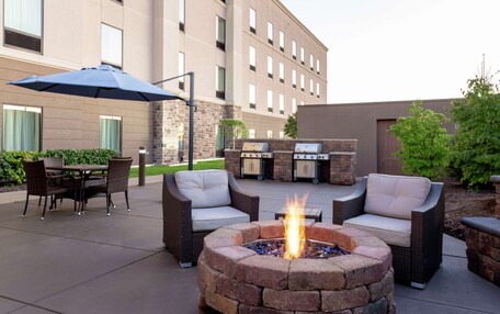 An outdoor patio with a fire pit, wicker furniture, and a grill area.