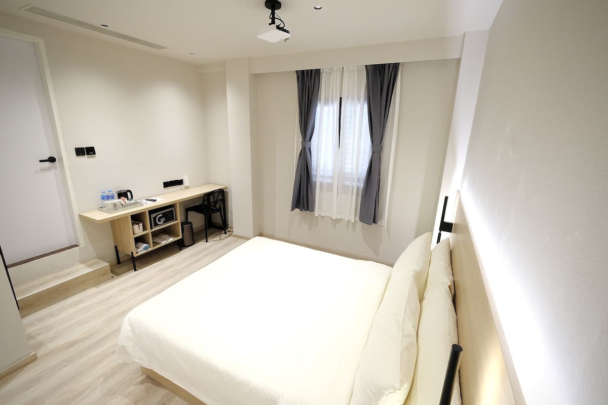 A bedroom with a bed, a desk, and a window with curtains.