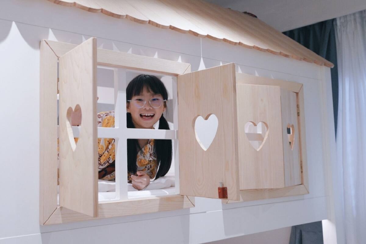 A wooden playhouse with heart-shaped cutouts and a child inside.