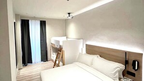 Una habitación de hotel moderna con una cama grande, una mesita de noche, un proyector en el techo y vistas al pasillo.