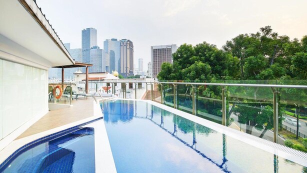 Piscina en la azotea con vista al horizonte de la ciudad, barandas de vidrio y un área de descanso.