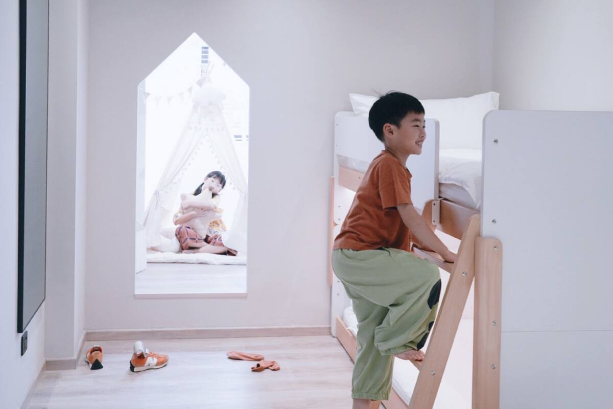 A child's bunk bed in a room with a window, a small window, and a wooden floor.