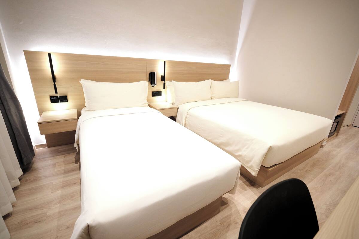 A hotel room with two beds, wooden headboards, bedside tables with lamps, and a black chair.