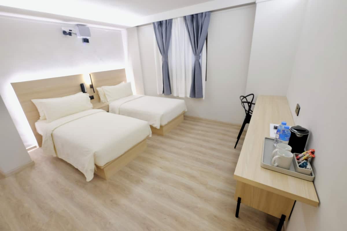 A hotel room with two beds, a desk with a tray of items, and a window with curtains.