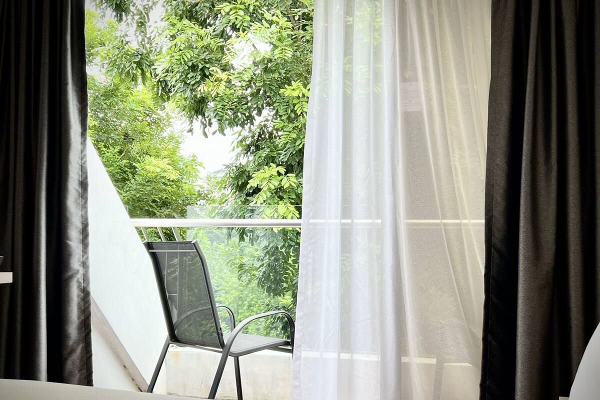 A room with a bed, a chair, and a window with sheer curtains.
