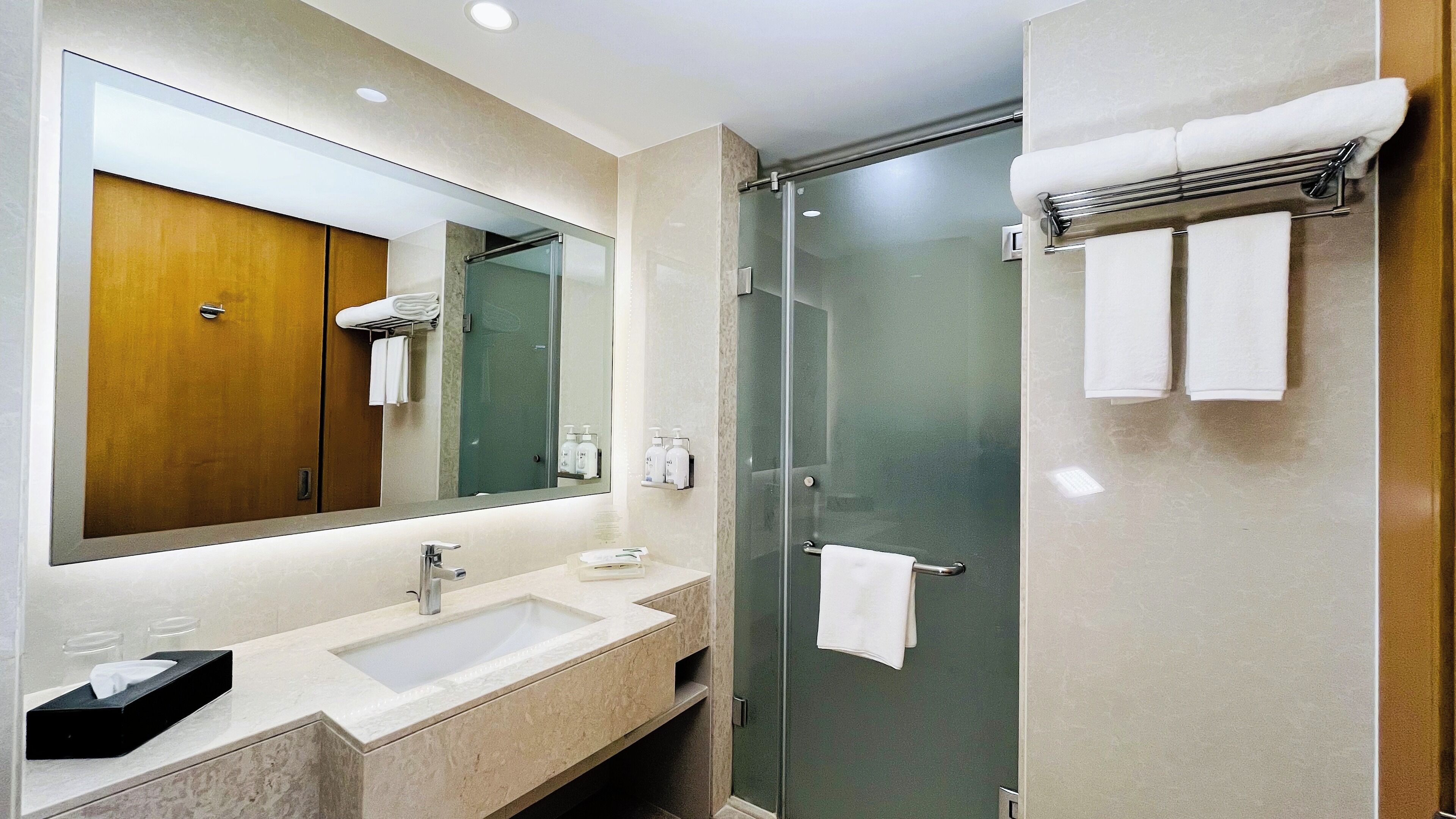 A modern bathroom with a large mirror, a sink, and a glass-enclosed shower.
