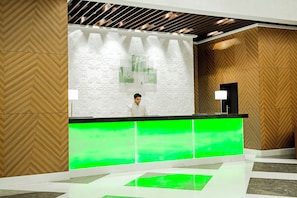 A reception area with a modern design, featuring a wooden herringbone pattern on the walls, a green illuminated reception desk, and a sign that reads "Holiday Inn." - Holiday Inn Amritsar Ranjit Avenue by IHG (Amritsar)