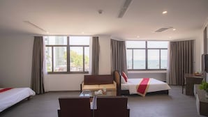 Ein Hotelzimmer mit zwei Betten, einem Sofa, einem Schreibtisch und großen Fenstern mit Blick.
