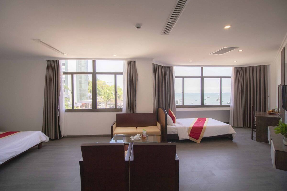 Une chambre d’hôtel avec deux lits, un canapé, un bureau et de grandes fenêtres donnant sur un paysage.