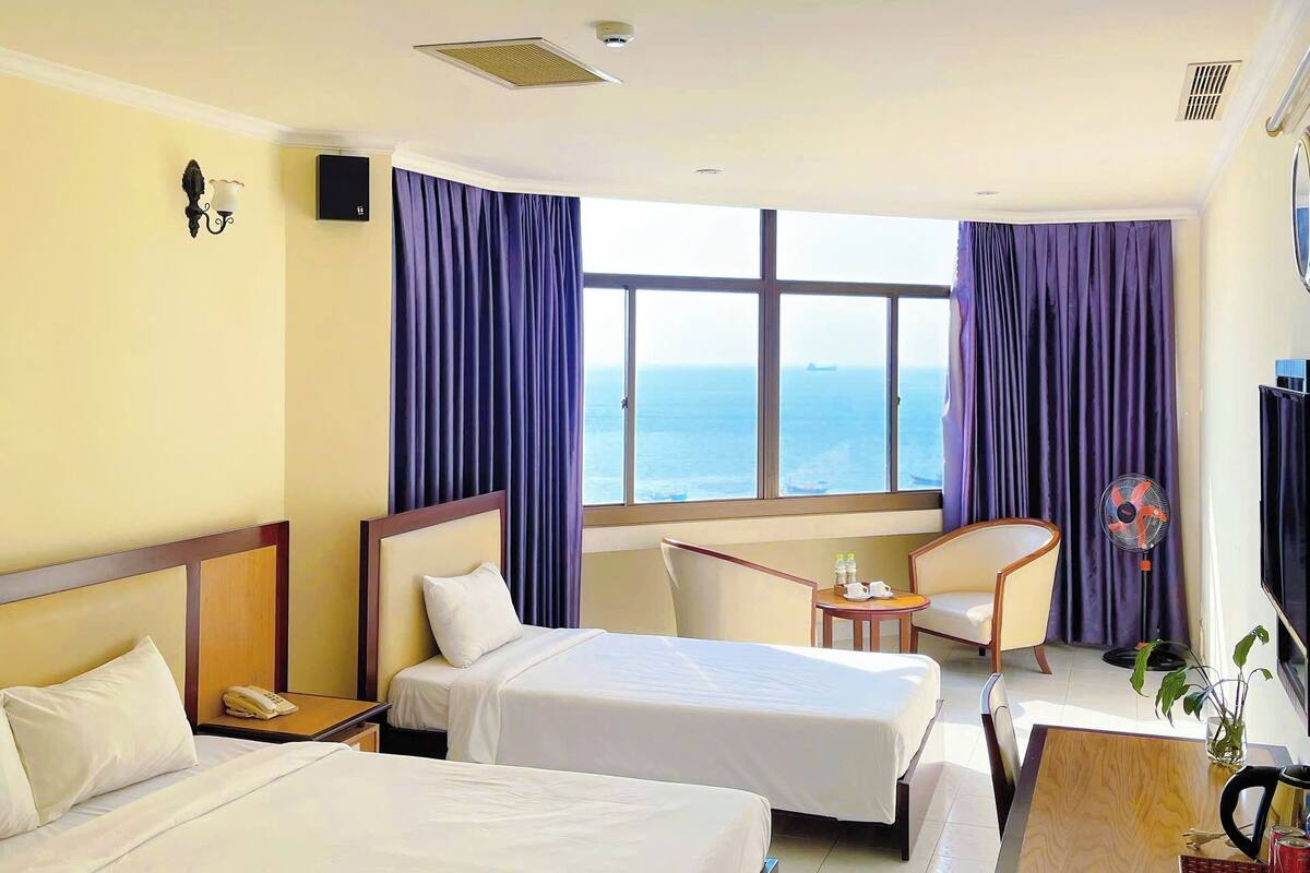 Une chambre d’hôtel avec deux lits, un bureau, une chaise, une télévision et une vue sur la mer.