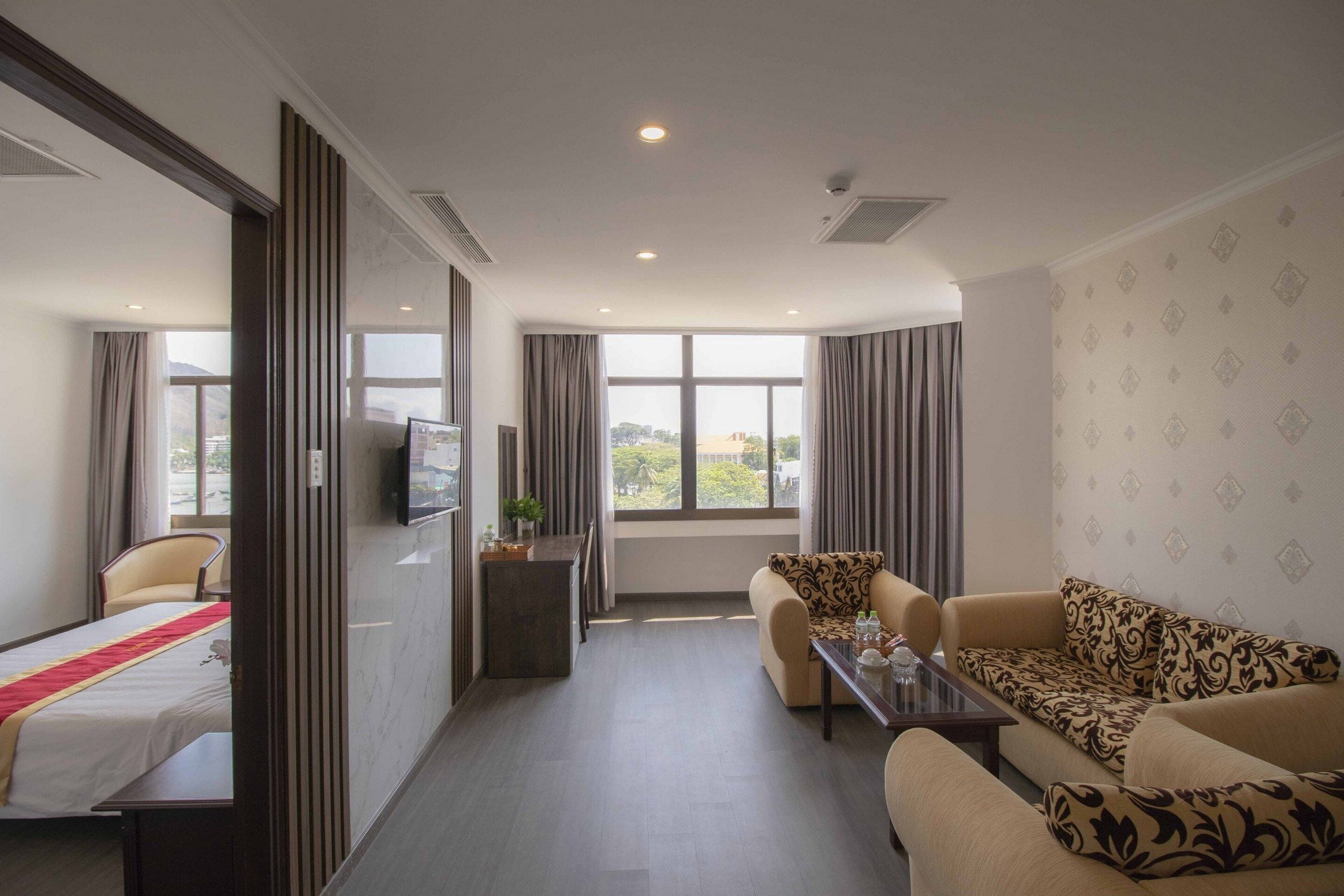 Ein Hotelzimmer mit Bett, Sofa, Fernseher, kleinem Tisch und einem Fenster mit Vorhängen.