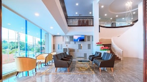 Eine großzügige Lobby mit modernem Design, ausgestattet mit einer Sitzecke mit Sofas und Sesseln, einem großen Flachbildfernseher an der Wand und einer Treppe zu einer oberen Ebene.