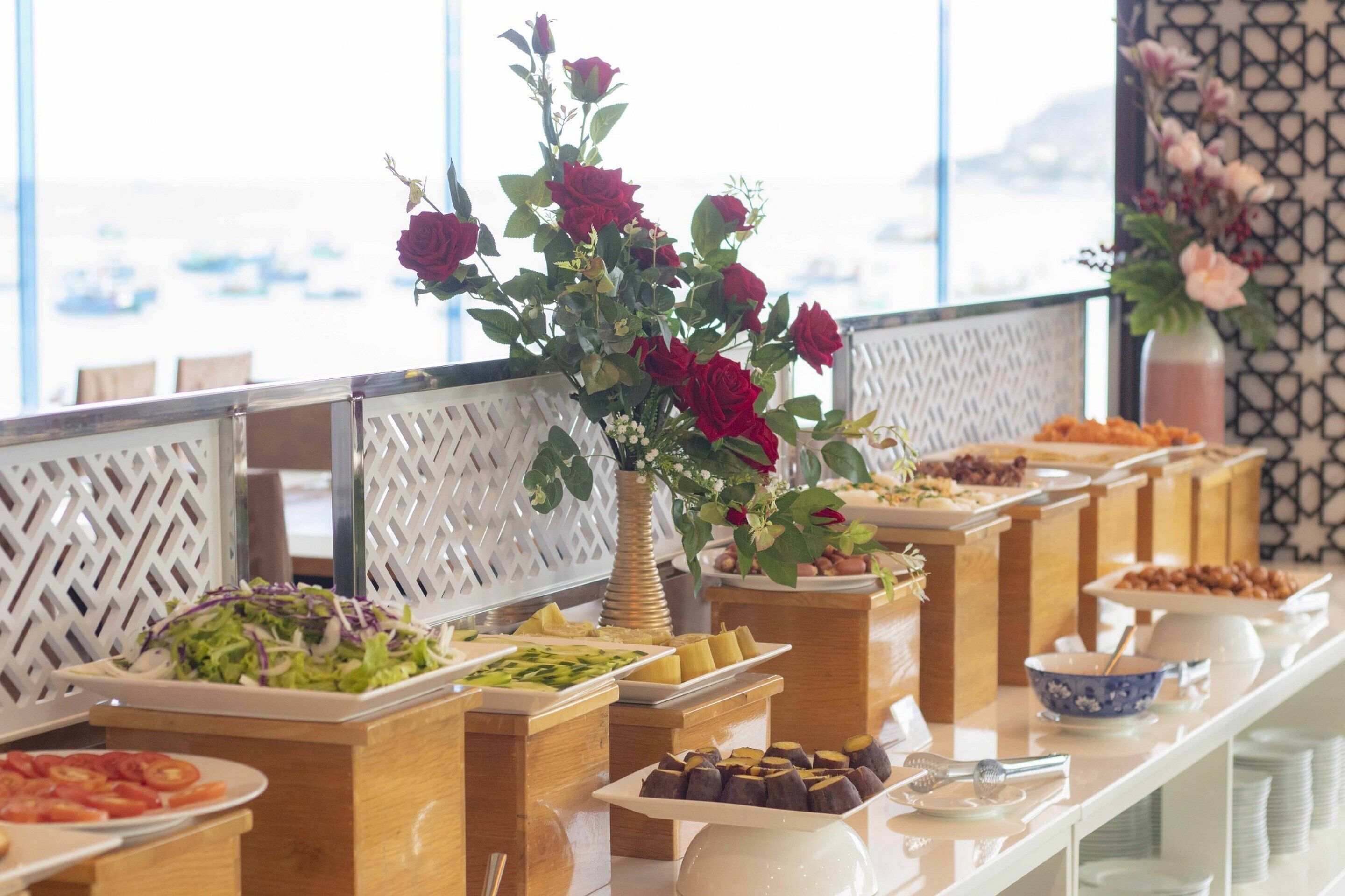 A buffet with various food items and a vase of red roses.