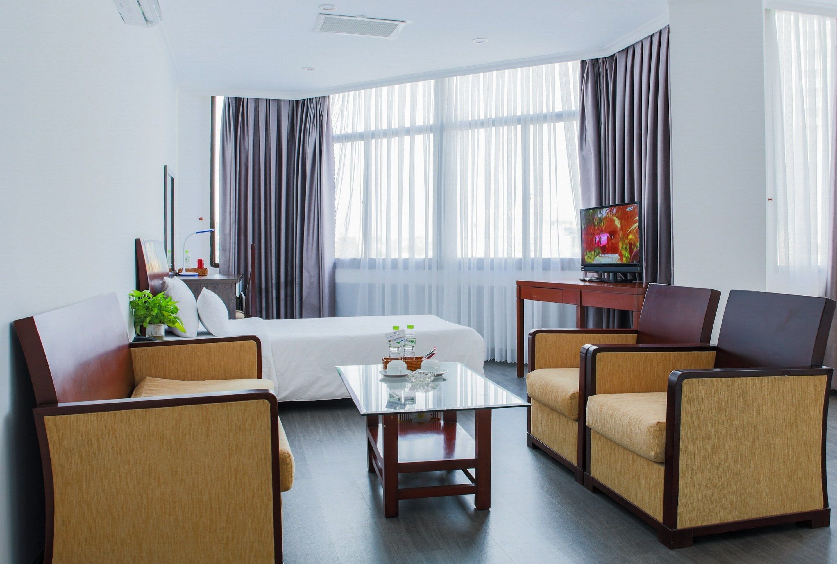 Una habitación de hotel con cama, televisión, mesita de café y dos sillones.