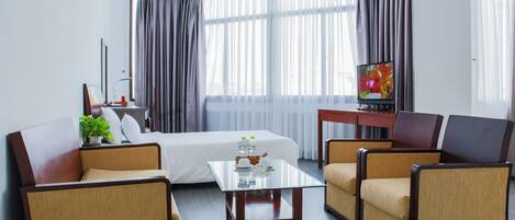 Una habitación de hotel con cama, televisión, mesita de café y dos sillones.