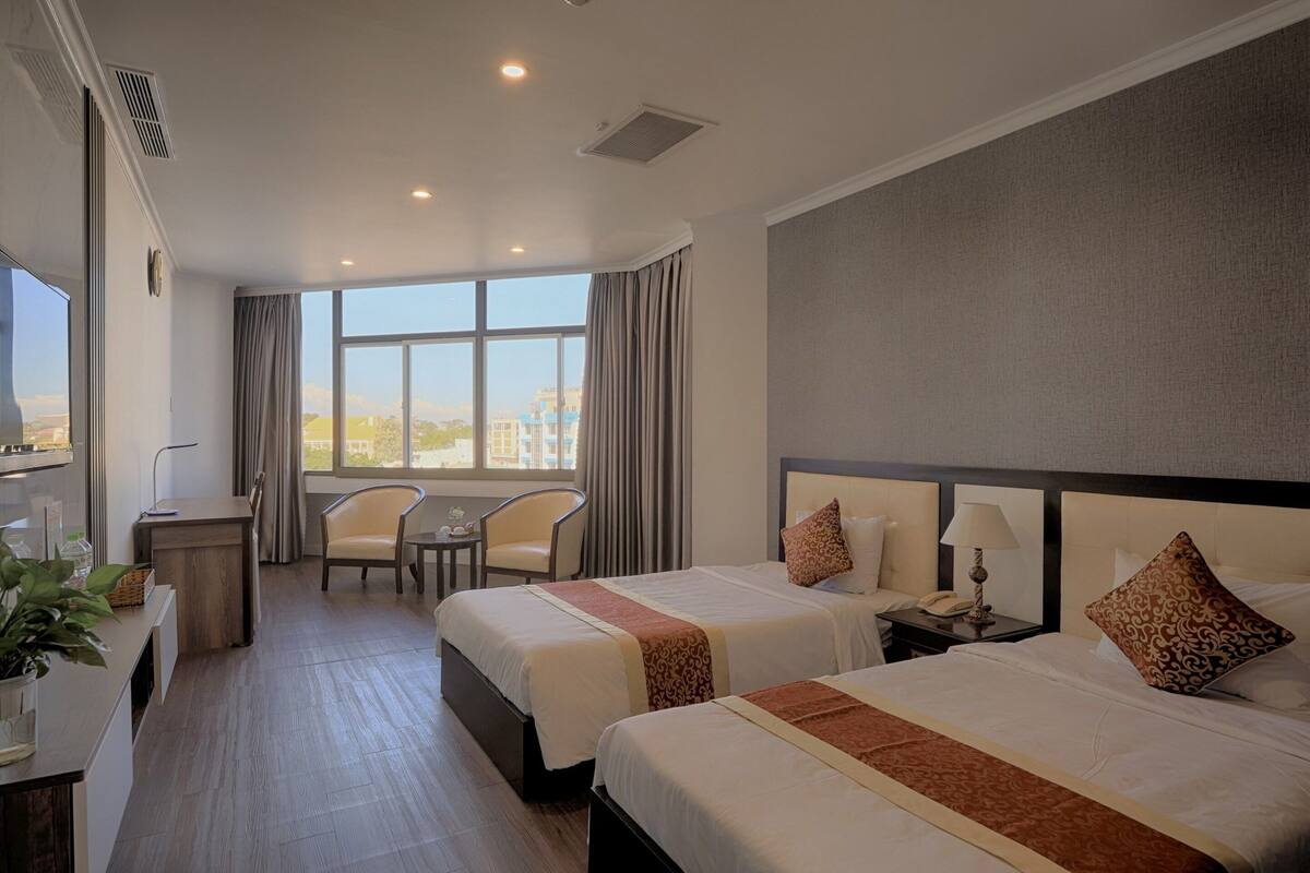Une chambre d’hôtel avec deux lits, un bureau, une chaise et une grande fenêtre donnant sur la ville.