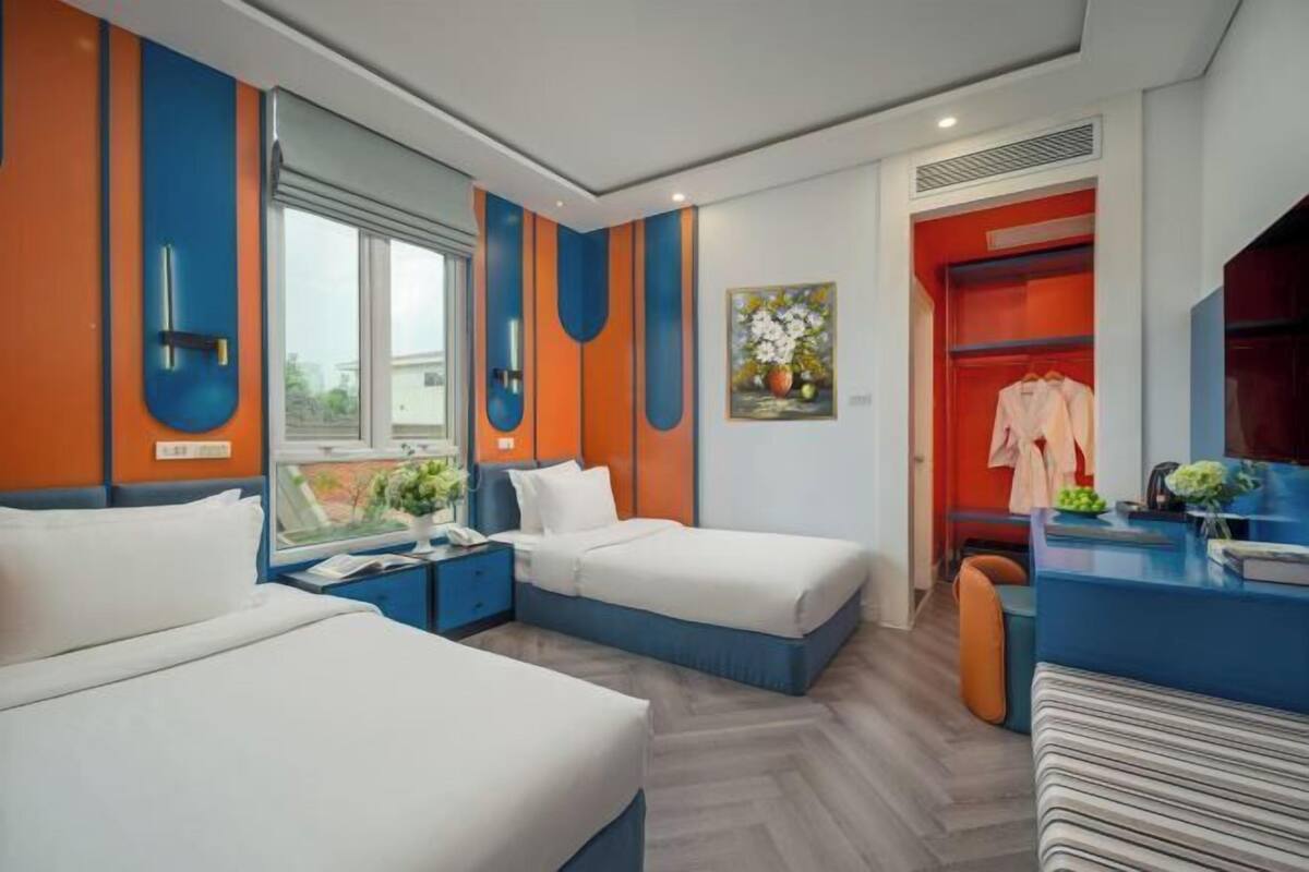 Une chambre d’hôtel moderne avec deux lits, un bureau et une armoire rouge.