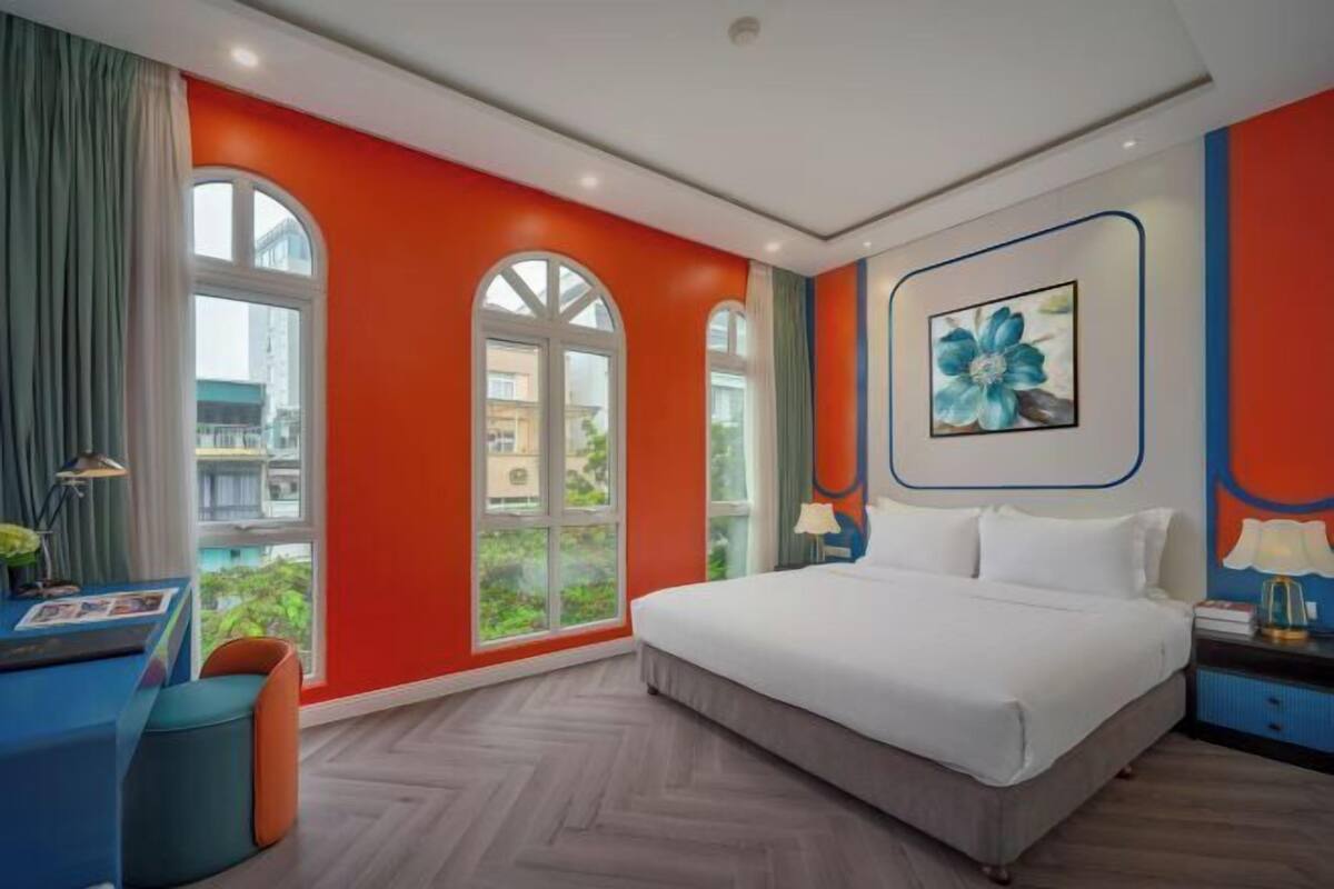 Une chambre d’hôtel moderne, dotée d’un grand lit, d’un bureau et offrant une vue sur la ville grâce à de grandes fenêtres.