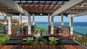 A wooden deck with a pool, surrounded by lush greenery, overlooking the ocean.