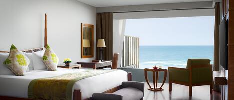 Habitación de hotel con una cama grande, una silla, una mesita, una lámpara y vista al océano.