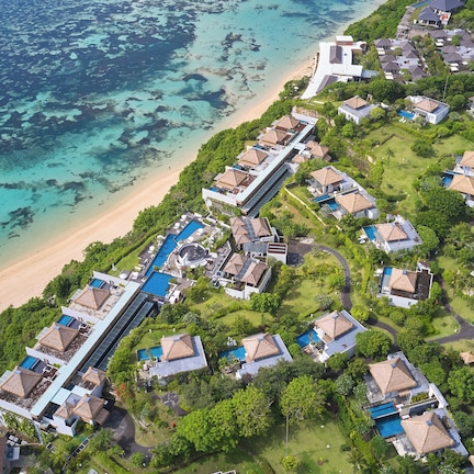 An aerial view of a resort with multiple bungalow-style buildings, a central pool area, and a beach adjacent to the ocean.