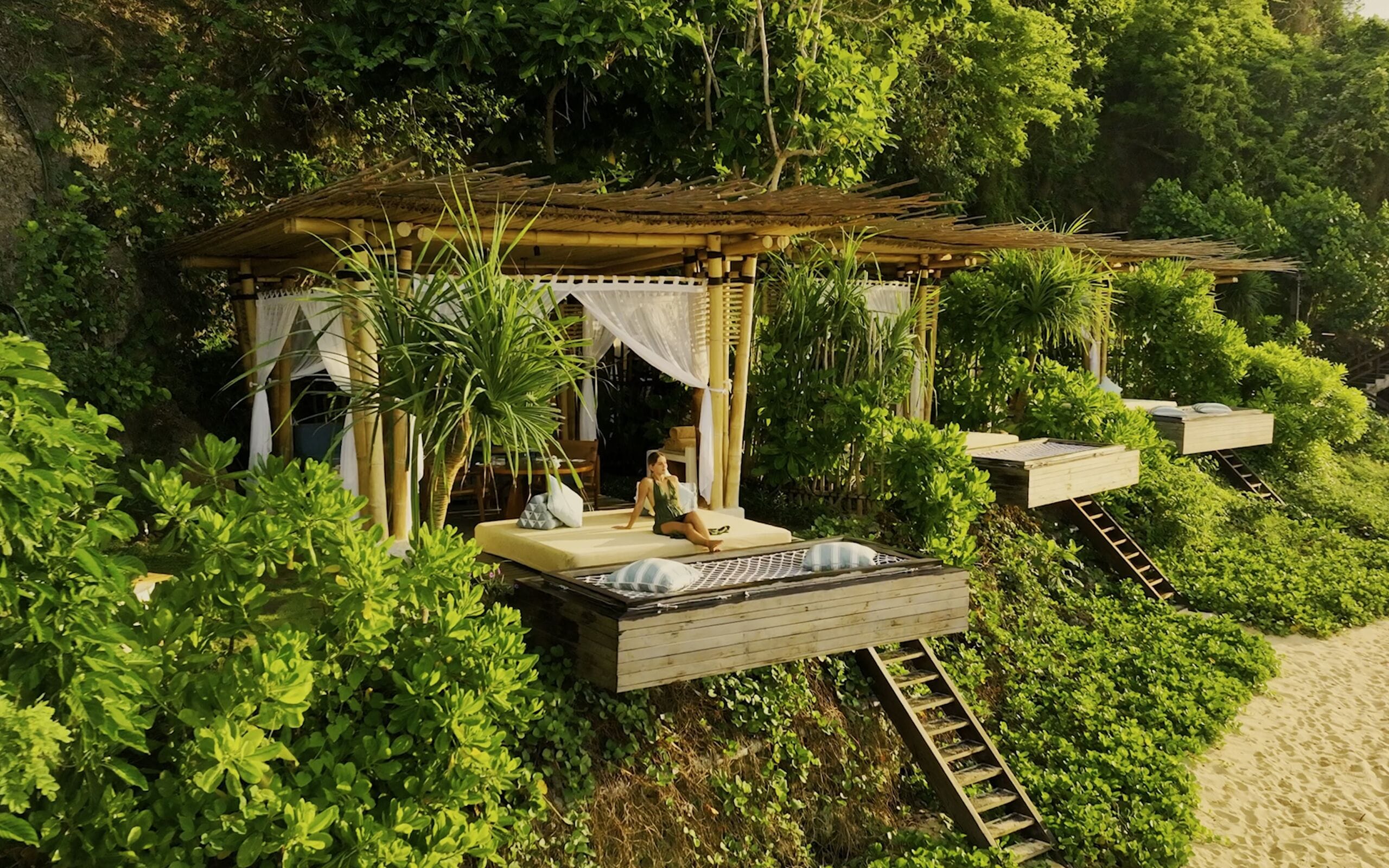 A secluded wooden structure with a thatched roof, surrounded by lush greenery and a sandy beach.