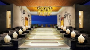Un interior moderno con una escalera que lleva a un balcón, con arte mural geométrico y jarrones decorativos.