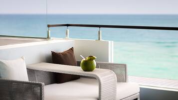 A balcony with a wicker sofa, a green vase with a straw, and a view of the ocean.